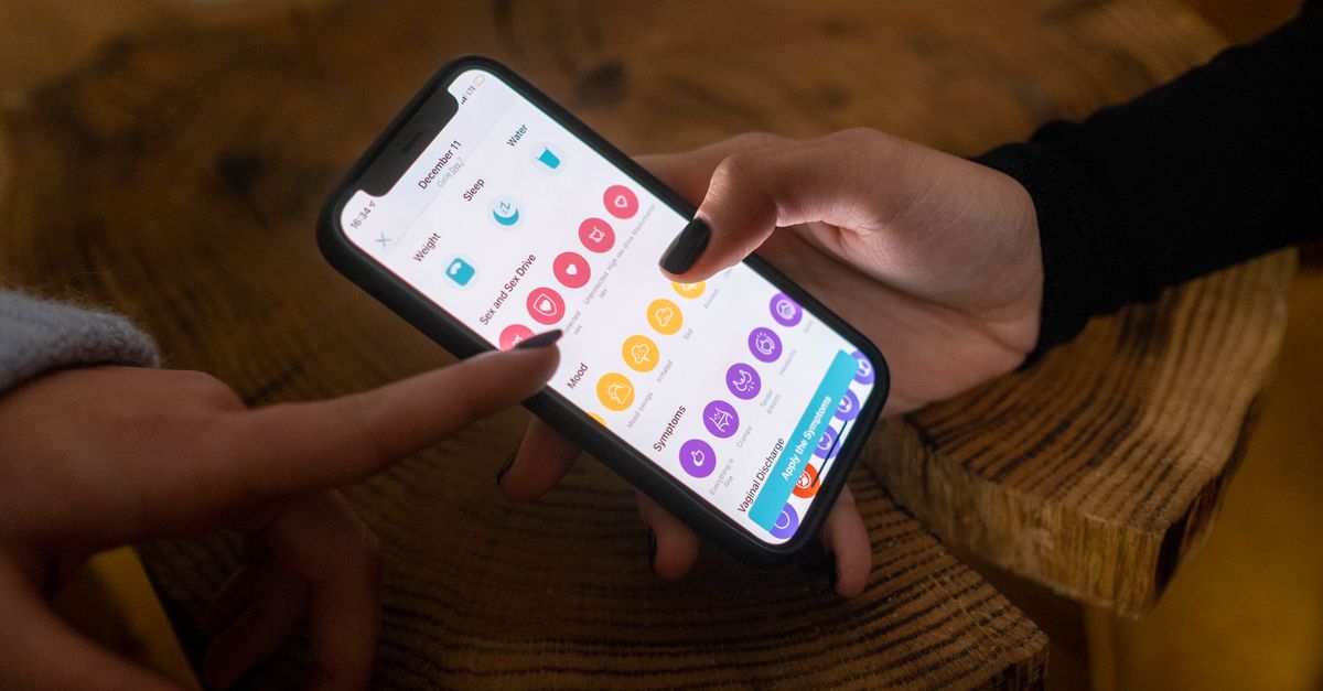Telefonunda adet takip uygulamasını açan bir kadının elini gösteren yakın çekim