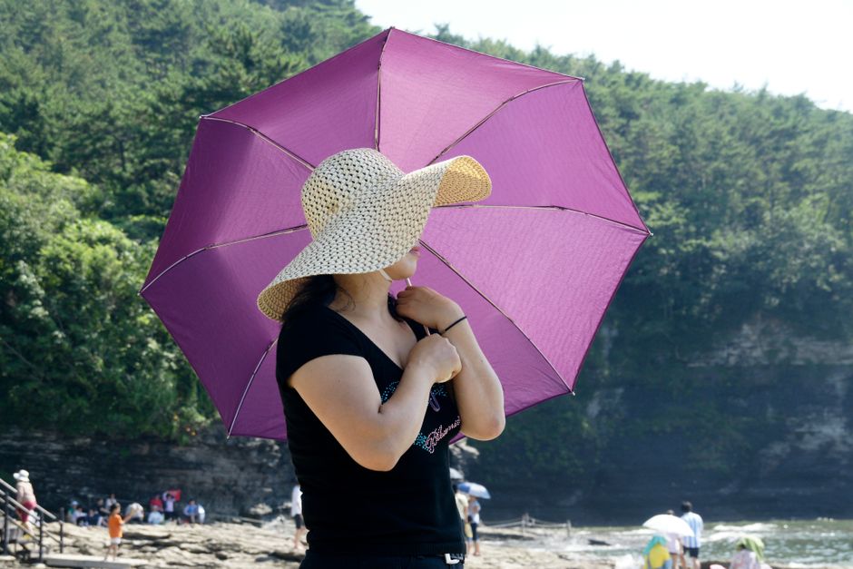 Plajda geniş kenarlı şapka ve şemsiyeyle güneşten korunan bir kişi